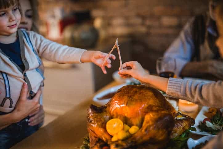 Little boy enjoying while having Thanksgiving dinner with his family and pulling a wishbone with his unrecognizable sibling.