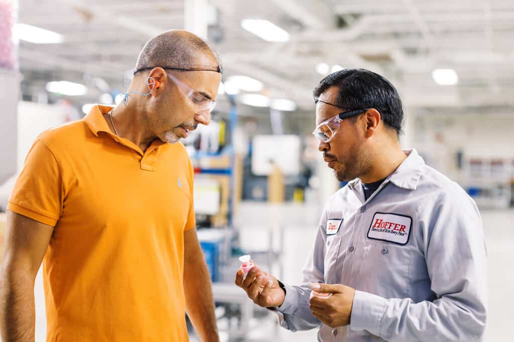 two men on factory floor looking at a plastic part