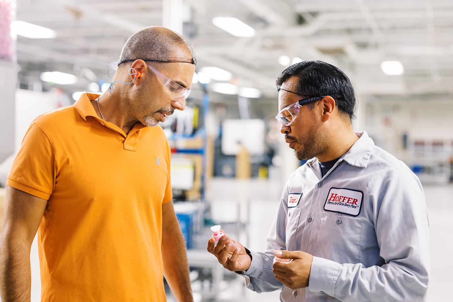 two men on factory floor looking at a plastic part